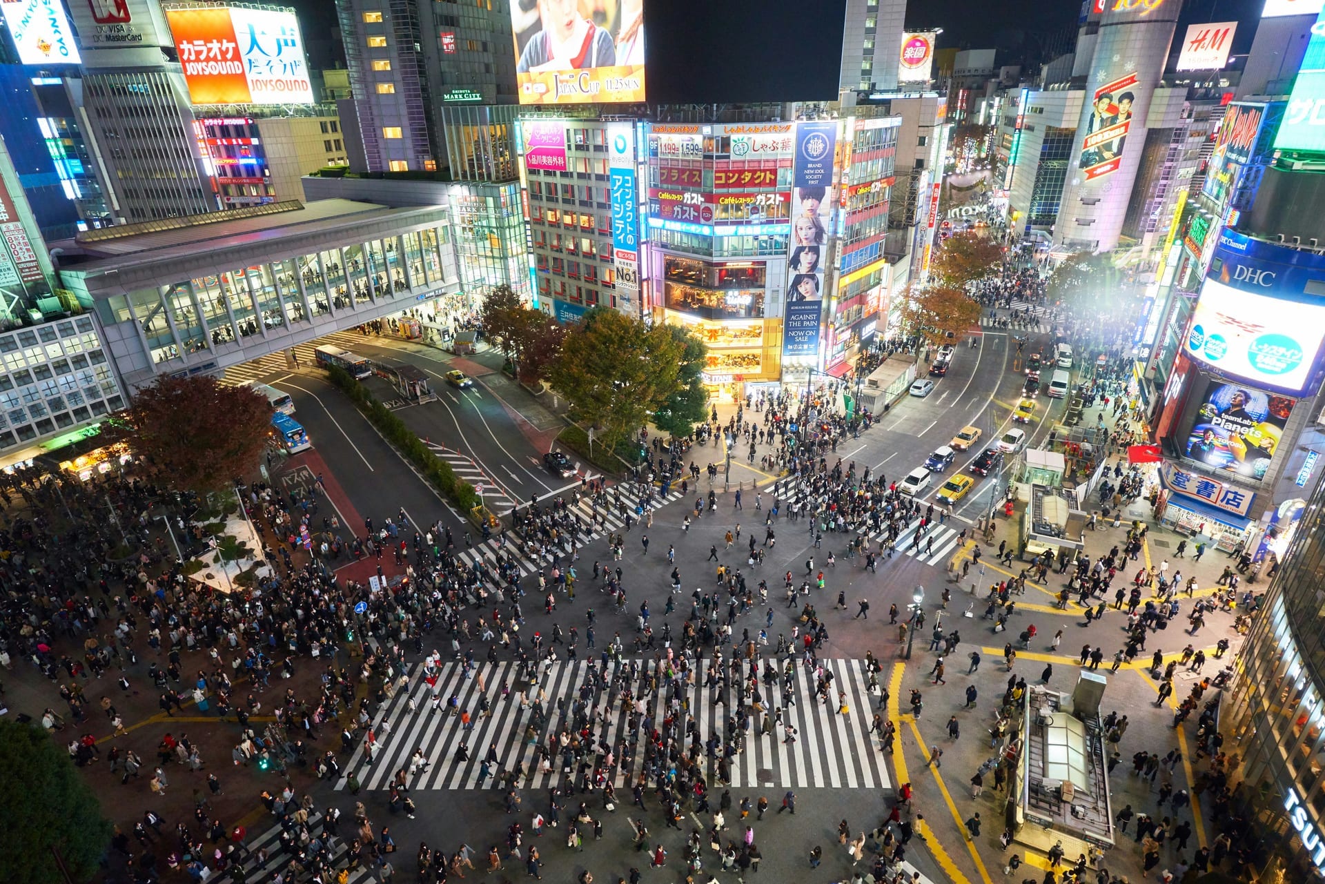 Aerial nighttime view of Shibuya Crossing showing pedestrians crossing in all directions surrounded by city lights